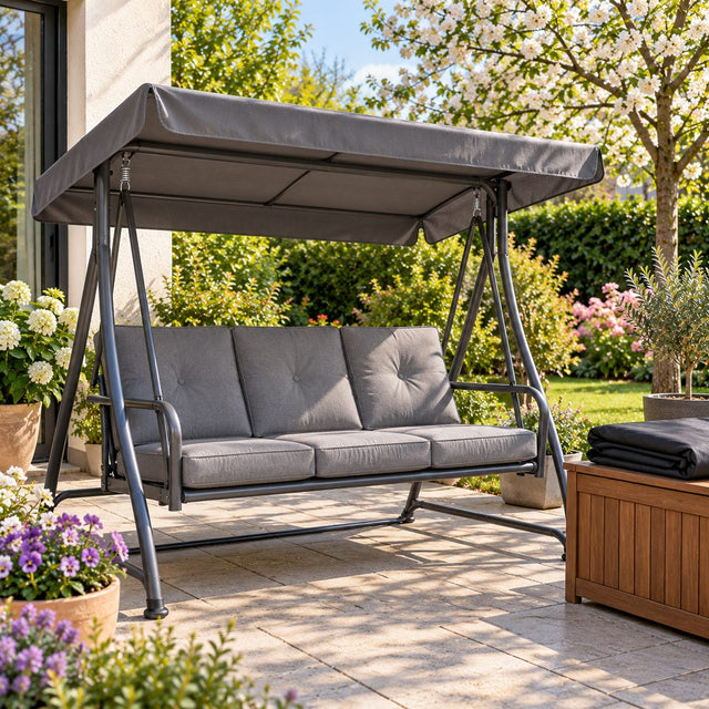 Balancelle de jardin au printemps avec une toile d’assise grise neuve bien tendue, housse noire pliée sur un coffre en bois à côté