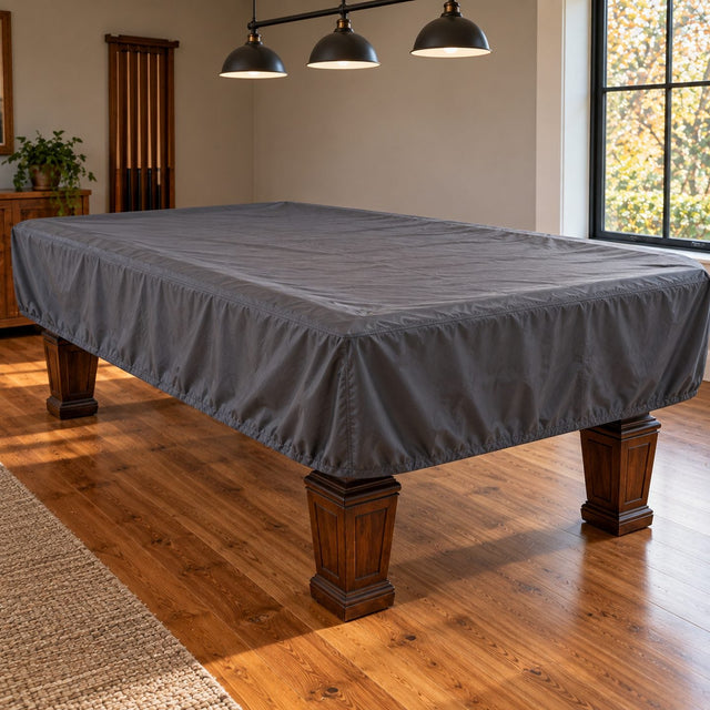 Table de billard recouverte d'une housse grise bien ajustée dans une salle de jeux calme, bandes visibles sous le tissu