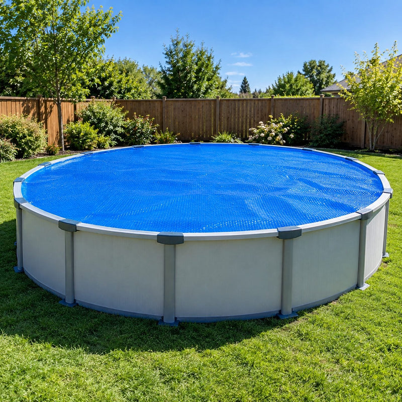 Piscine ronde hors sol entièrement couverte d’une bâche à bulles bleue en plein soleil, avec pelouse et palissade en bois