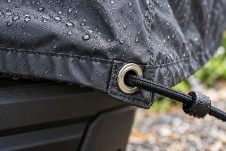 Gros plan d'un œillet renforcé et d'un sandow sur le bord d'une housse imperméable sous la pluie